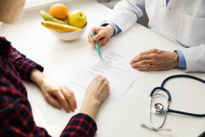 Doctor consulting patient with diet chart and fresh fruits on table, discussing personalized nutrition and health goals.
