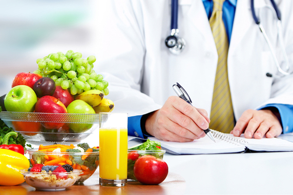 Doctor writing nutrition plan with fresh fruits, vegetables, and juice on the table promoting healthy diet and lifestyle